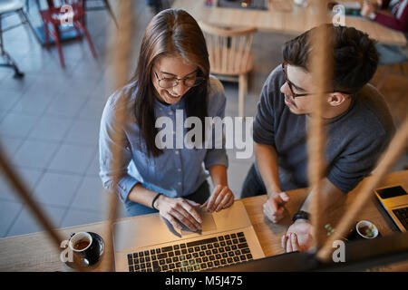Junge Mann an lächelnde Frau in einem Café mit Laptop suchen
