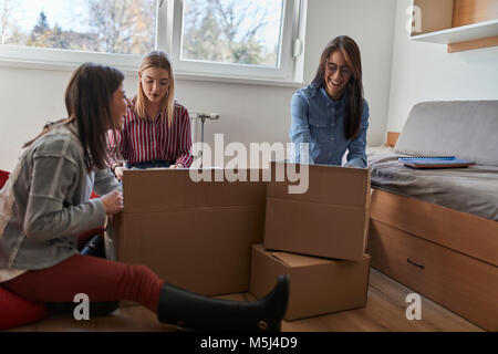 Drei glückliche junge Frauen Auspacken der Kartons in einem Zimmer Stockfoto