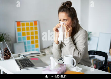 Kranke Frau zu Hause am Schreibtisch ihre Nase weht Stockfoto