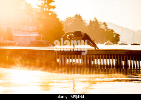 Frau praktizieren Yoga auf Steg am See Stockfoto