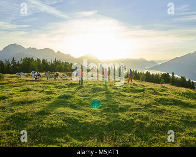 Österreich, Tirol, Mieminger Plateau, Wanderer auf alpine Weide mit Kühen bei Sonnenaufgang Stockfoto