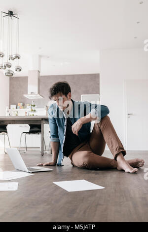 Junger Mann sitzen auf dem Boden in einem Loft mit Laptop Stockfoto