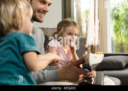 Lächelnd Vater und Kinder im Toy model ship Suchen auf der Couch zu Hause Stockfoto