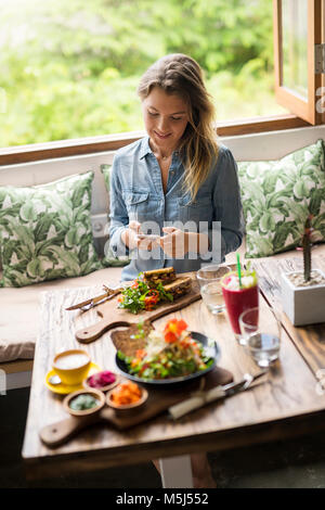 Frau ein Bild von Essen mit Smartphone im gemütlichen Cafe vor Fenster Stockfoto