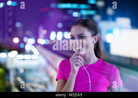 Lächelnden jungen Frau in Rosa sportshirt Musik in der Stadt in der Nacht hören Stockfoto