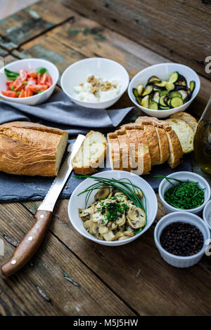 Bruschetta und verschiedenen Zutaten, Brot, Tomaten, Zucchini, Käse, Ricotta, Walnüsse, Pilze, Kräuter, Basilikum, Schnittlauch Stockfoto