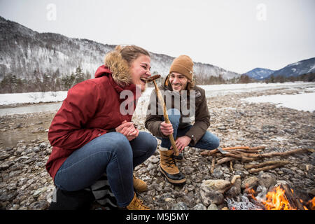 Glückliches Paar auf einer Reise im Winter essen ein Würstchen am Lagerfeuer. Stockfoto