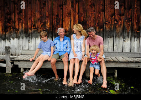 Familie zusammen sitzen auf Jetty spritzen mit Wasser Stockfoto