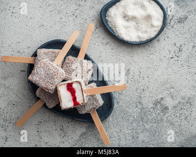 Hausgemachte raw lamington Eis springt auf grauem Hintergrund. Australische süße Nachspeise lamington mit Chia und Himbeeren Marmelade, Schokolade und Kakao. Stockfoto