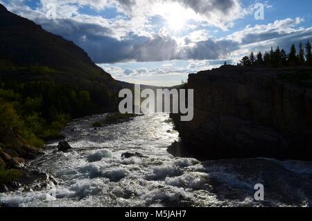 Ein kleiner Berg Fluss, fließt schnell down stream, über scharfe, schroffe Felsen, während die Sonne in der Ferne steigt der Dampf von unten spiegeln Stockfoto