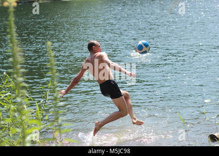 Mutige muskulösen Mann in den See spielen mit dem Ball im Wasser Stockfoto