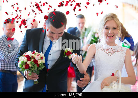 Auf die Braut und der Bräutigam werfen sie Rosenblätter. Braut und Bräutigam glücklich in Rosenblättern Stockfoto