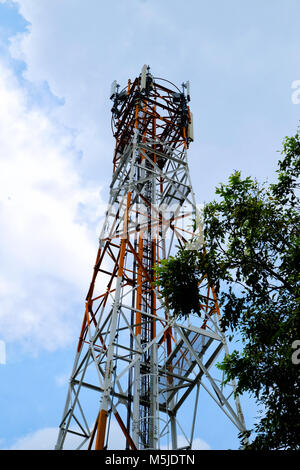 Rote und weiße Signal tower Struktur stehen vor dem blauen Himmel mit Grüner Baum Stockfoto