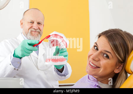 Reife männliche Zahnarzt zeigen, wie Zähne richtig zu putzen, zu den weiblichen Patienten Stockfoto