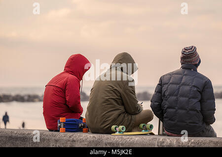San Sebastian, Spain-February 21,2018: Skater sitzen auf der Wand des zurriola heißen Mate genießen, während whatsappean, Gros - donostia Stockfoto