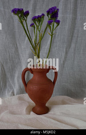 Sterbende blaue Blumen in einer Vase Terrakotta, auf einem musselin Tuch gegen ein spucktuch Hintergrund. Stockfoto