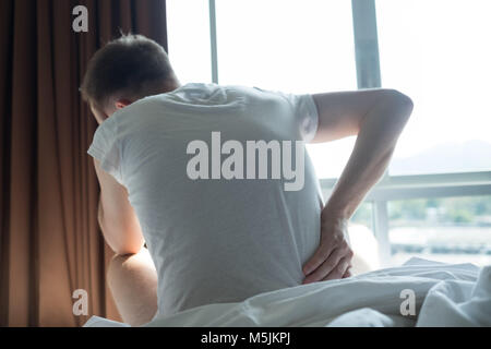 Junge Mann sitzt innen auf dem Bett Gefühl Schmerz in seinem Rücken Stockfoto