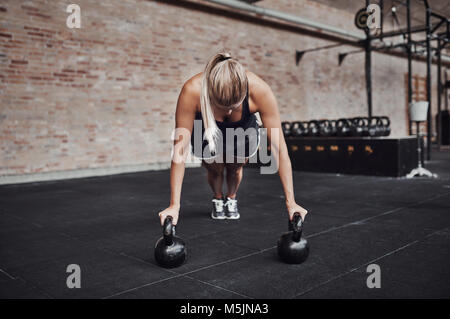 Passen junge blonde Frau in sporstwear pushups Tun mit Gewichten, während Sie arbeiten allein auf dem Boden einer Turnhalle Stockfoto