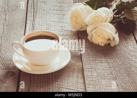 Weich ausgewachsenen weißen Rosen mit Tasse schwarzen Kaffee auf Holzbrett mit kopieren. Getönten Bild. Close Up. Selektive konzentrieren. Stockfoto