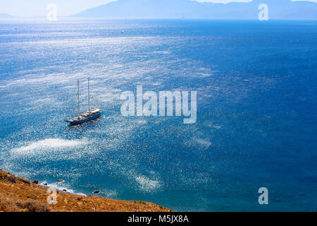 Schöne Küste mit Segelboot im tiefblauen Wasser, blauer Himmel und die Silhouette der Insel am Horizont Stockfoto