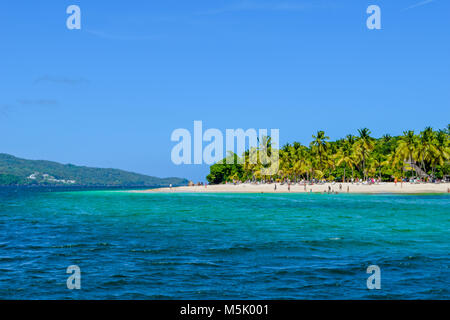 Schöner Strand mit Palmen, blauer Himmel und türkisfarbenem Wasser, einige Touristen Spaß haben, entspannen und schwimmen im Meer, Karibik Stockfoto