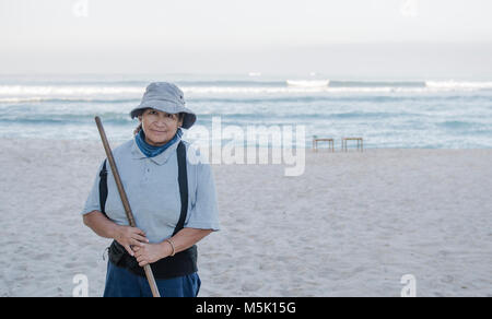 Ältere lächelnden und freundlichen mexikanischen Frau arbeitet an einem Strand geharkt und Reinigung iup den Sand Stockfoto