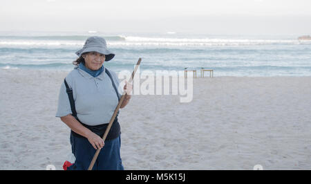 Ältere lächelnden und freundlichen mexikanischen Frau arbeitet an einem Strand geharkt und Reinigung iup den Sand Stockfoto