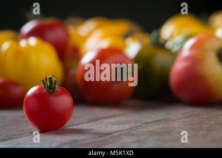 Kirschtomate auf rustikalen Holzmöbeln Hintergrund mit bunten Tomaten im Hintergrund. Geringe Tiefenschärfe. Stockfoto