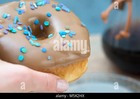 Eine Hand mit einem köstlichen maple Donut und Kaffee/Teekocher Stockfoto