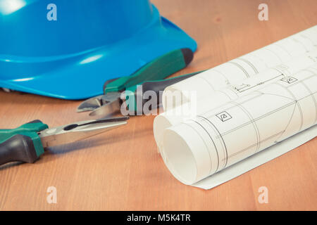 Rollen von Diagrammen oder elektrischen Konstruktionszeichnungen, Schutzhelm und Werkzeuge für Ingenieur Jobs liegen im Schreibtisch Stockfoto