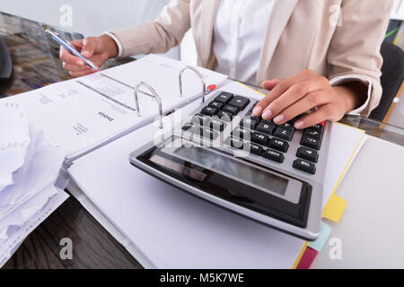 Nahaufnahme der Geschäftsfrau Hand Berechnung Rechnung mit Rechner am Schreibtisch im Büro Stockfoto