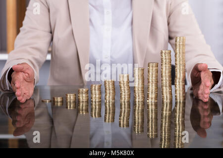 Nahaufnahme der Geschäftsfrau Hände schützen Gestapelte Münzen auf Tisch Stockfoto