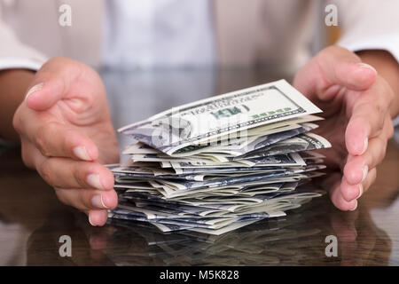 Nahaufnahme der Geschäftsfrau schützende Hand Stapel Hundert-Euro-Scheine auf dem Schreibtisch im Büro Stockfoto