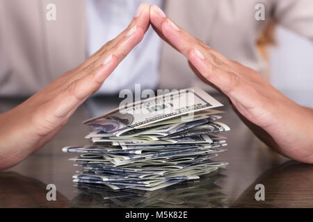 Nahaufnahme der Geschäftsfrau schützende Hand Stapel Hundert-Euro-Scheine auf dem Schreibtisch im Büro Stockfoto