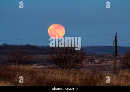 Große silberne leuchtende Mond close-up auf dunklen blauen Himmel mit vereinzelten Wolken. Neue Vollmond in der Nacht über Horizont mit Büschen und Leistungskabel lin Stockfoto