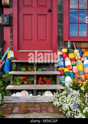 Rote Tür Eingangsbereich mit bunten Bojen, Blumen, Muscheln, und cloud Spiegelungen im Fenster am Hafen in Rockport MA. Stockfoto