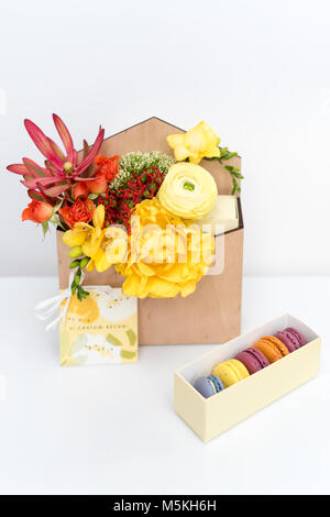 Geschenkset mit Blumen und Süßigkeiten. Makronen und Feder Blumenstrauß in Holzkiste auf weißem Hintergrund. Stockfoto