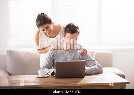 Junge lächelnde Paar an Laptop zu Hause Suchen Stockfoto