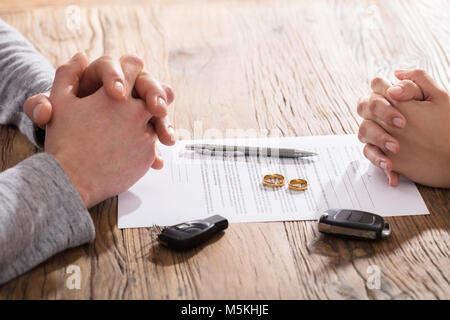 Hände auf Scheidung Dokument mit Hochzeit Ringe und Autoschlüssel auf den Tisch Stockfoto