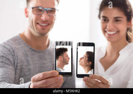 Lächelnde junge Paar zeigen Ihre Handy mit ihren Fotos auf dem Bildschirm Stockfoto