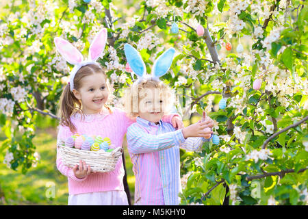 Kinder mit Hasenohren auf Ostereiersuche im Blooming Cherry Blossom Garten. Kleinen Jungen und Mädchen mit Frühling Blumen und Eier Warenkorb im Obstgarten. C Stockfoto