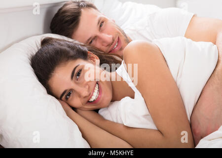 Liebevollen Lächelnden jungen Paar liegend auf Bett Stockfoto