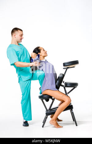 Thema Massage und Büro. jungen männlichen Therapeuten in blauen Anzug, Rückenmassage mit sein Knie in den Rücken der weiblichen Arbeitnehmer verspannt, business Frau in s Stockfoto