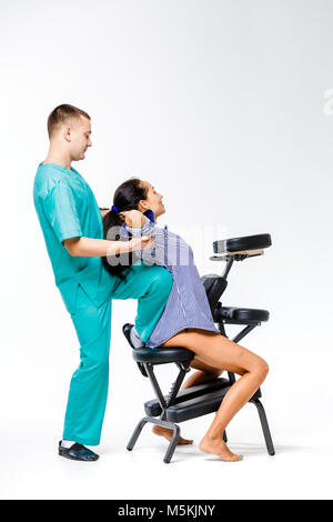 Thema Massage und Büro. jungen männlichen Therapeuten in blauen Anzug, Rückenmassage mit sein Knie in den Rücken der weiblichen Arbeitnehmer verspannt, business Frau in s Stockfoto