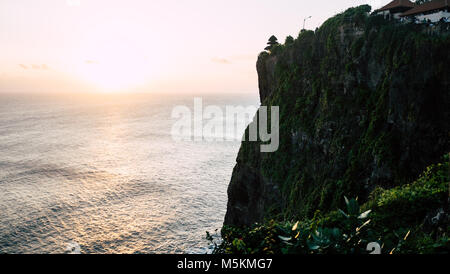 Der Sonnenuntergang über dem Meer von einem Tempel auf den Klippen in Uluwatu, Bali gesehen Stockfoto