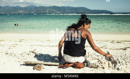 Eine gebräunte Frau spielt im Sand am Strand in den Gili Inseln, Bali Stockfoto