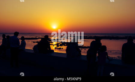 Eine Gruppe von Menschen beobachten Sie den Sonnenuntergang über dem Meer von der Waterfront in Mumbai, Indien Stockfoto