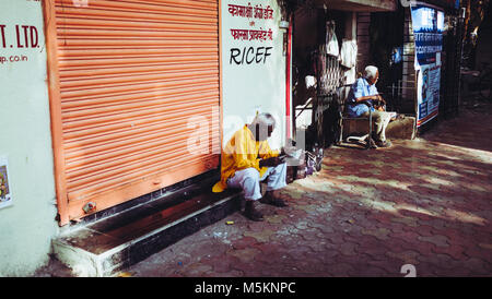 Ein Mann außerhalb eines Shop mit den Fensterläden in Mumbai, Indien sitzen Stockfoto