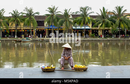 Eine Frau sitzt am Fluss Wasser vor Verkauf von Obst und Gemüse in Hoi An, Vietnam Stockfoto