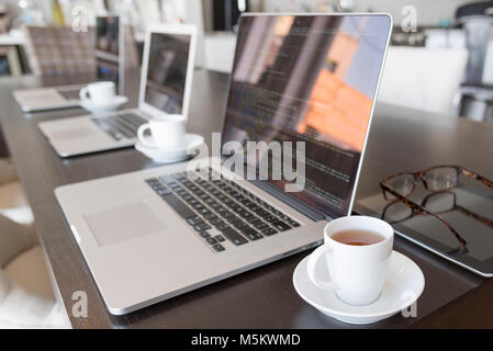 Mehrere Computer mit Kaffee in einer Büroumgebung niedrigen Winkel mit Code auf dem Bildschirm. Stockfoto